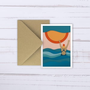 May include: A paper cut-out illustration of a person swimming in the ocean. The person is wearing a blue swimsuit and a red swim cap. The ocean is blue and green, and the sun is orange and red. The background is a light pink.