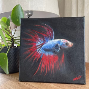 May include: A painting of a blue and red betta fish with a black background. The fish is swimming with its fins spread out. The painting is signed in the bottom right corner.