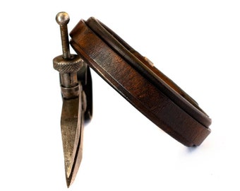 May include: A vintage leather belt with a metal tool attached to it. The belt is brown and the tool is silver.