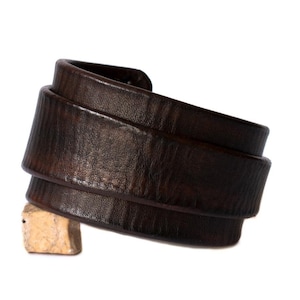 May include: A brown leather cuff bracelet with a textured surface.