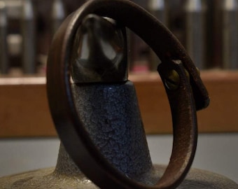 May include: A brown leather bracelet with a silver buckle. The bracelet is on a gray textured surface.