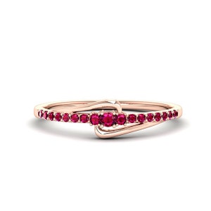 May include: A delicate rose gold ring with a single row of small red gemstones. The ring features a unique design with a curved band and a small cluster of gemstones at the centre.