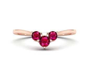 Könnte beinhalten: Ein Ring aus Roségold mit drei Rubin-Steinen, die in einem geschwungenen V-förmigen Design gefasst sind.