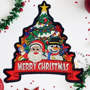 Puede incluir: Parche navideño bordado con Papá Noel y un muñeco de nieve frente a un árbol de Navidad decorado. El parche tiene un borde negro y una pancarta roja que dice "MERRY CHRISTMAS".