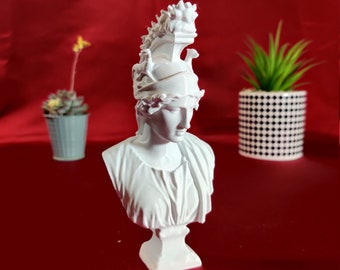 May include: White bust sculpture of a woman wearing a helmet with a decorative design. The sculpture is on a red surface.