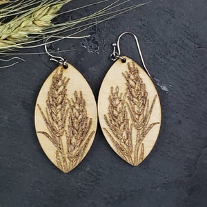 Peut inclure: Une paire de boucles d'oreilles en bois avec un motif de tiges de blé découpé au laser. Les boucles d'oreilles sont de forme ovale et ont une couleur bois naturelle.
