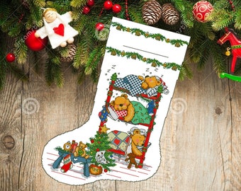 May include: A white Christmas stocking with a red and green design featuring three teddy bears sleeping in a bunk bed. The stocking has a blank space at the top for a name. The stocking is on a wooden background.