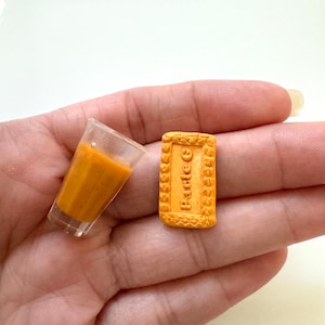 Op de afbeelding: Een miniatuur glas sinaasappelsap en een miniatuur koekje met de tekst "Parle-G" erop.