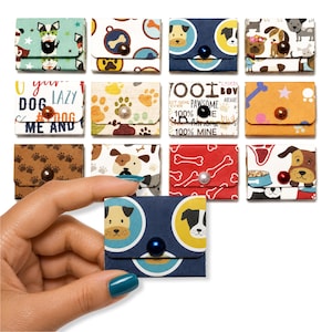 May include: A collection of small, rectangular paper envelopes featuring various dog-themed patterns, including paw prints, bones, and cartoon dog faces. Each envelope is secured with a single, centered, round bead button in assorted colors.