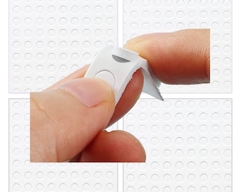 May include: A white sheet with a grid of small, round, adhesive dots. A hand is peeling back a strip of the adhesive dots.