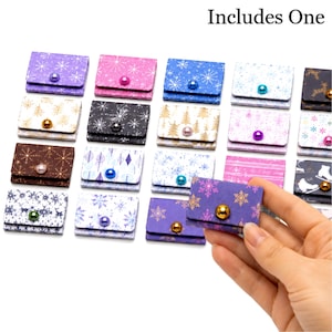 May include: A collection of small, rectangular, folded paper pouches featuring various holiday-themed patterns including snowflakes, trees, and skates. Each pouch is secured with a single, colorful, round bead acting as a button closure.