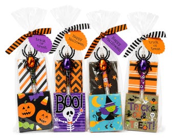 May include: Four clear plastic gift bags containing a Halloween-themed pen topped with a plastic spider and a small rectangular notepad. Each bag is tied with a striped ribbon and a tag reading Happy Halloween or trick or treat.