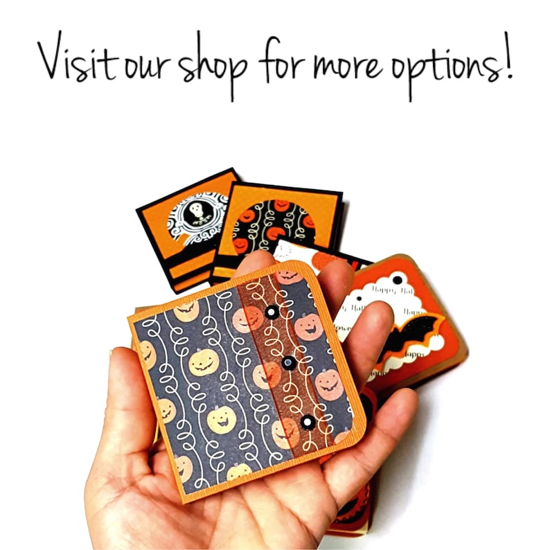 Op de afbeelding: Een hand houdt verschillende vierkante kaarten met Halloween-thema vast met oranje, zwarte en witte ontwerpen. De kaarten bevatten pompoenen, vleermuizen en andere griezelige afbeeldingen. De tekst op de afbeelding luidt: "Visit our shop for more options!"