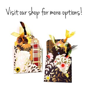 May include: Two decorative gift tags with a layered design featuring floral and leaf patterns in shades of brown, gold, and pink. The tags are tied with ribbon and have a scalloped edge.