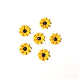 May include: Six yellow paper sunflower embellishments with black centers are arranged on a white background. The sunflowers have layered petals and are a bright, cheerful craft supply.