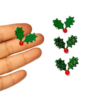May include: Three green glitter holly leaves with red berries. The holly leaves are in a traditional Christmas design.