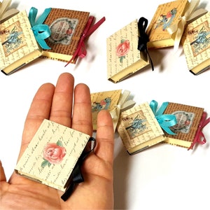 May include: A set of miniature, decorative, paper-bound books with vintage floral and bird illustrations. Each book has a ribbon tied around it in a variety of colors, including pink, blue, and white.