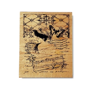 May include: A rectangular wooden stamp with a vintage design. The stamp features a woman's profile, butterflies, musical notes, and decorative elements in black ink. The background has a distressed, aged appearance.