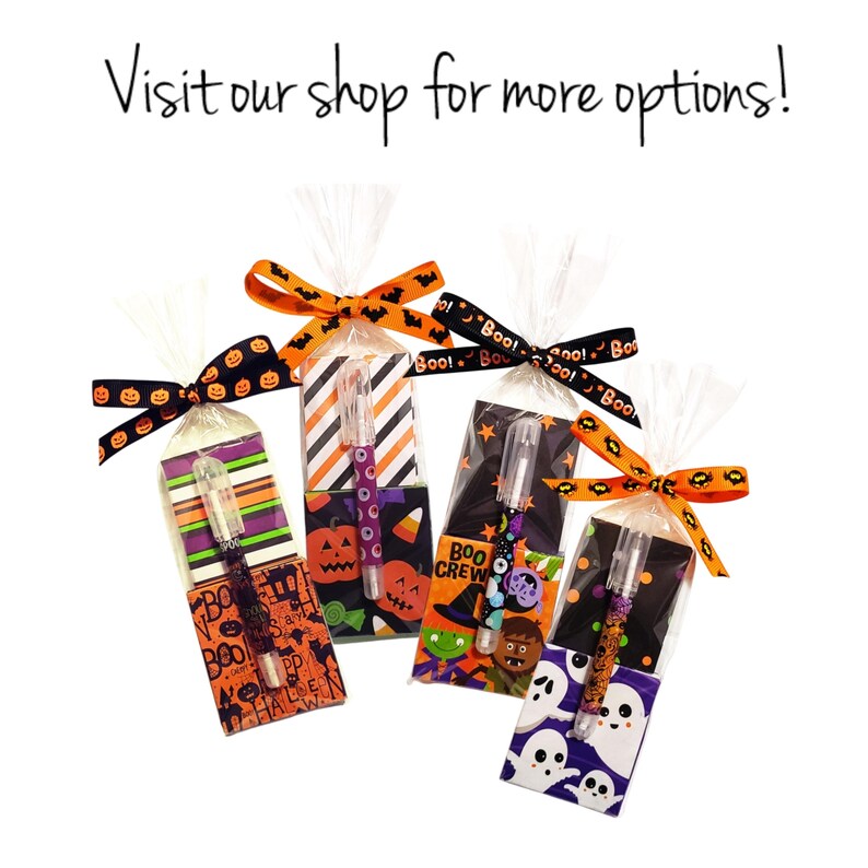 Op de afbeelding: Vier Halloween-thema pennen in cellofaan zakjes, elk met een decoratieve strik. De pennen hebben verschillende ontwerpen, waaronder pompoenen, geesten en strepen. De tekst "Visit our shop for more options!" is zichtbaar.