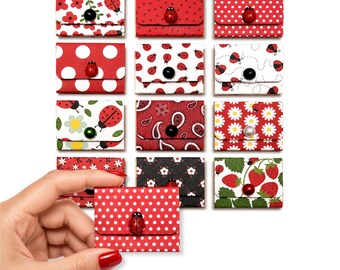 May include: A collection of thirteen small, rectangular, envelope-style pouches featuring various patterns including ladybugs, polka dots, flowers, strawberries, and paisley. Each pouch is secured with a small, round, decorative button closure.