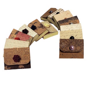 May include: A set of ten small, decorative boxes with a vintage aesthetic. Each box is covered in patterned paper with a different design, including floral patterns, script, and a brown floral pattern. Each box has a small button embellishment.