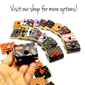 May include: A selection of small, decorative Halloween-themed boxes with diverse patterns, including polka dots, bats, and pumpkins. Each box has a button closure and some feature a small rose. The text "Visit our shop for more options!" is visible.