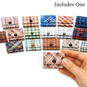 May include: A collection of small, square, envelope-style pouches featuring various plaid and checkered patterns in multiple colors. Each pouch has a single button closure. The text 'Includes One' is visible at the top of the image.