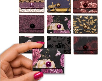 May include: A collection of ten small, rectangular paper envelopes featuring various dark floral and patterned designs. Each envelope is secured with a single, centered, round bead-like button in colors including gold, purple, black, and deep red.