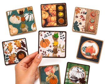 May include: Seven square coasters featuring autumn-themed designs with pumpkins, fall leaves, and plaid patterns. Each coaster has a dark brown border. One coaster is held up, displaying a white background with pumpkins, berries, and twine.