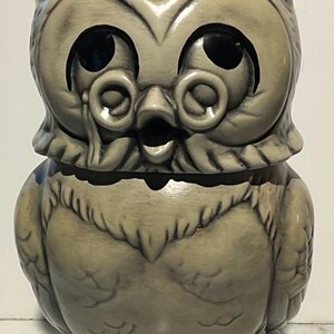 May include: A ceramic owl figurine wearing a graduation cap and glasses. The owl is painted in a light gray color and has a whimsical expression.