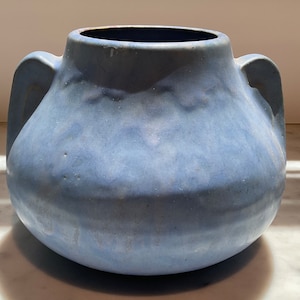 May include: A blue ceramic vase with two handles. The vase has a rounded body and a slightly flared rim.