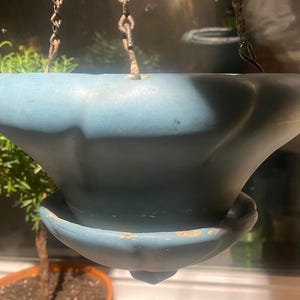 May include: A light blue ceramic hanging planter with a scalloped rim and a saucer. The planter is suspended by two chains.