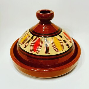 Op de afbeelding: Een terracotta tajine met een bruine glazuur en een decoratief ontwerp van gele, rode en zwarte cirkels. De tajine heeft een deksel en een basis.