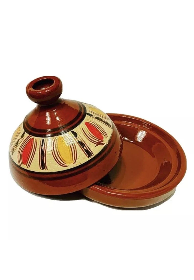 May include: A brown ceramic tagine with a lid. The lid has a white background with a decorative pattern of red, yellow, and black lines and shapes.
