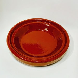 May include: A terracotta dish with a glazed interior. The dish has a rounded shape and a slightly raised rim.