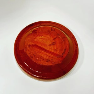 May include: A round, terracotta-colored plate with a glossy finish. The plate has a slightly raised rim and a smooth, even surface.