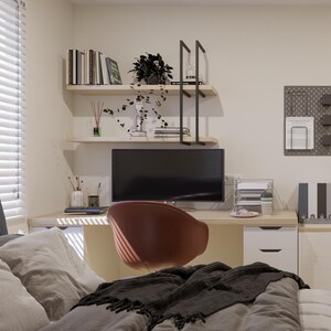 May include: A home office setup featuring a light wood desk with a computer monitor, a brown chair, and white drawer units. Above the desk are two floating shelves with books and a plant. A dark grey pegboard with office supplies hangs on the wall.