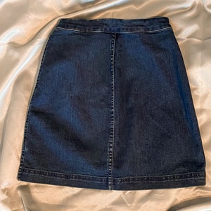 Op de afbeelding: Een donkerblauwe denim rok met een klassiek A-lijn silhouet. De rok heeft een knoopsluiting, een achternaad en een afgewerkte zoom. De stof lijkt een medium-gewicht denim te zijn.