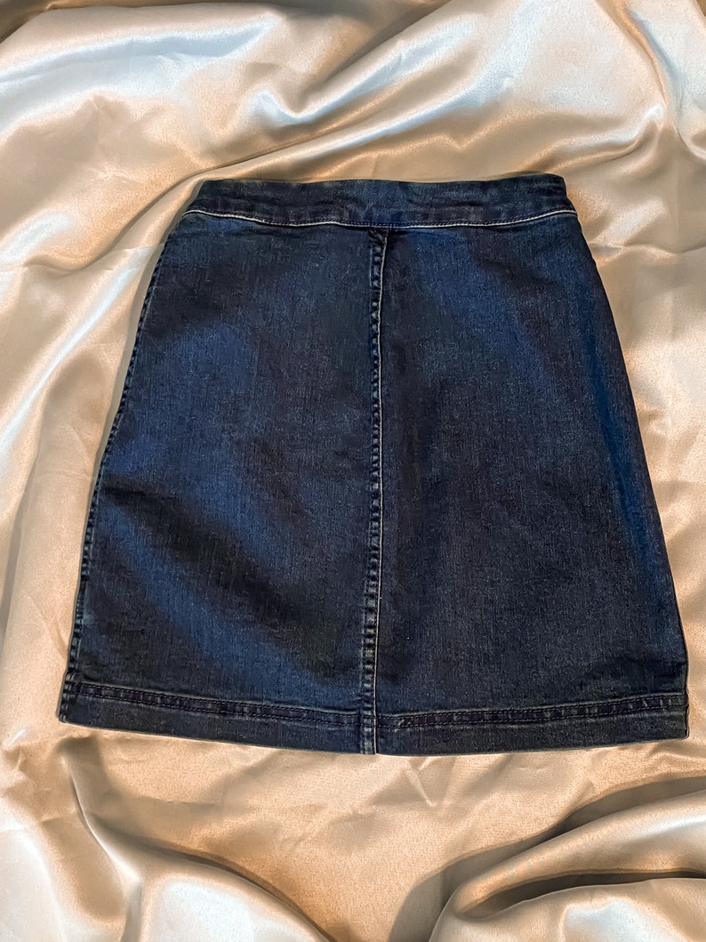 Op de afbeelding: Een donkerblauwe denim rok met een klassiek A-lijn silhouet. De rok heeft een knoopsluiting, een achternaad en een afgewerkte zoom. De stof lijkt een medium-gewicht denim te zijn.