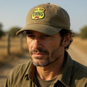 May include: Olive green baseball cap with the text "EST. 1930 EWING OIL" in yellow and white. The cap is worn by a person wearing an olive green button-down shirt.