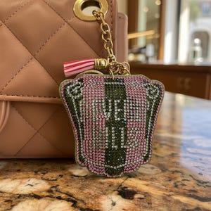 May include: A pink and green rhinestone keychain with the text "YES ONLY". The keychain is attached to a gold chain and a pink and white tassel. The background includes a pink quilted purse.