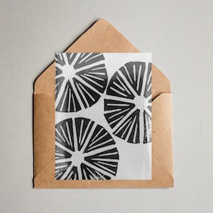 May include: A white card with a black and white geometric design of three overlapping circles with radiating lines. The card is in a brown envelope.