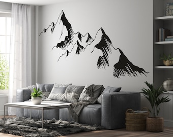 May include: A black and white mountain range wall decal with a minimalist design. The decal is applied to a white wall in a living room setting with a gray couch and a coffee table.