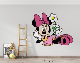 May include: A black and white cartoon illustration of Minnie Mouse wearing a pink dress and a pink bow. She is holding a white flower with a green stem and has a happy expression on her face.