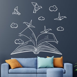 Puede incluir: Un sofá azul con cojines naranja y azul frente a una pared azul oscuro con un dibujo blanco de un libro abierto con pájaros de origami volando.