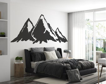 May include: A black and white mountain range wall decal with a minimalist design. The decal is applied to a white wall above a black leather bed with gray bedding.