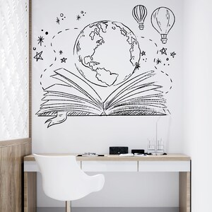 Puede incluir: Una pared blanca con un dibujo en blanco y negro de un libro abierto con un globo terr&aacute;queo en su interior. El libro est&aacute; rodeado de estrellas y globos aerost&aacute;ticos. Un escritorio blanco con una silla blanca est&aacute; frente a la pared.