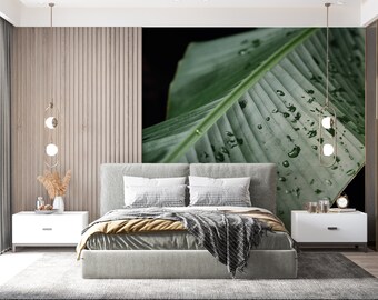 Könnte beinhalten: Ein modernes Schlafzimmer mit einem großen Bett, zwei weißen Nachttischen und einem großen Wandbild mit grünen Blättern. Das Bett hat ein graues Kopfteil, weiße und gemusterte Kissen und eine graue Decke. Der Raum hat eine neutrale Farbpalette.