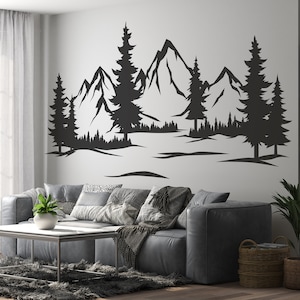 Può includere: Sagoma di adesivo da parete in bianco e nero di una catena montuosa con pini. L'adesivo è su una parete bianca in un soggiorno con un divano grigio e un tavolino da caffè.