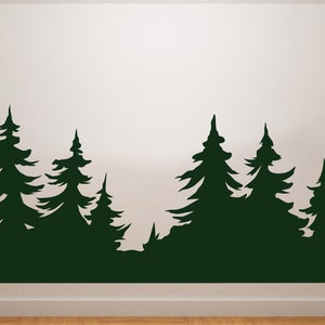 Op de afbeelding: Een muursticker met een silhouet van een bos met meerdere dennenbomen. De bomen zijn donkergroen en de achtergrond is wit.